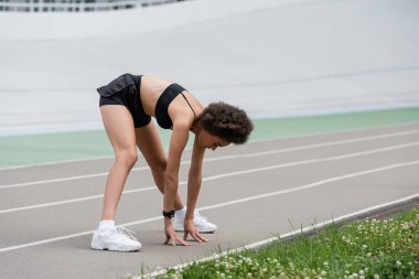 Young african american sportswoman stretching and touching running track on stadium 