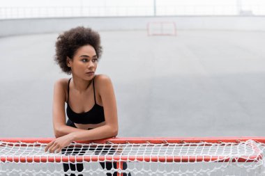 African american sportswoman in top standing near football goal on stadium 