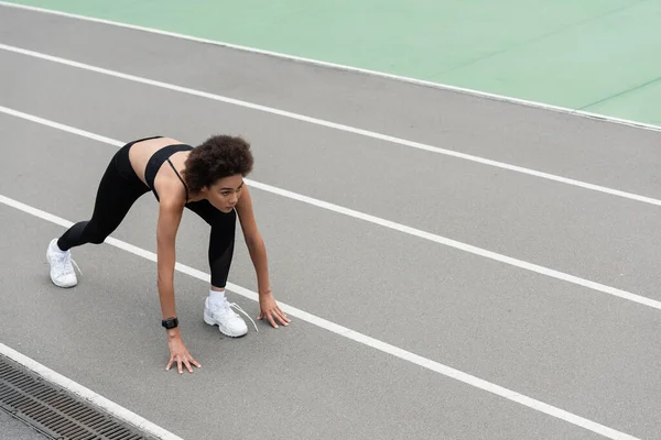 high angle view of african american runner standing in low start pose on track