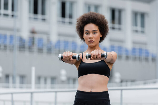 young african american sportswoman looking at camera while exercising with dumbbells