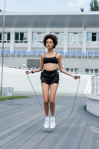 African american sportswoman training with jump rope on stadium at daytime