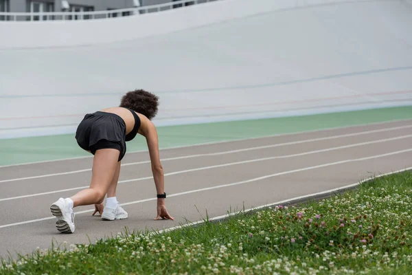 Back view of african american sportswoman standing in starting pose on running track