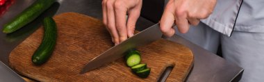 cropped view of chef cutting cucumber on wooden cutting board, banner