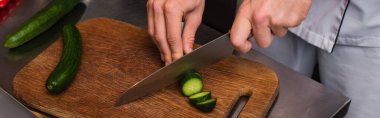 cropped view of chef cutting cucumber on wooden cutting board, banner clipart