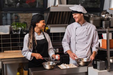 cheerful interracial chefs holding raw eggs while cooking together in kitchen 