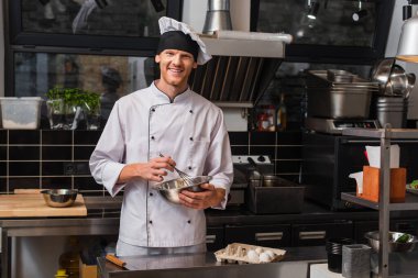 smiling chef whisking eggs and looking at camera near egg box
