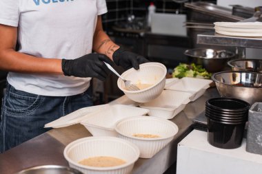 partial view of tattooed african american volunteer holding plastic bowl with soup in kitchen