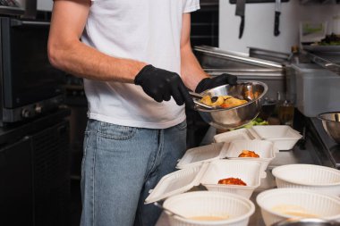 cropped view of social worker in latex gloves holding bowl with prepared food near plastic containers