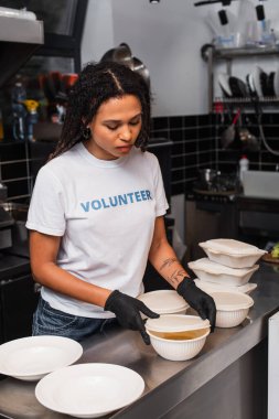 tattooed african american social worker covering plastic container with cup in kitchen