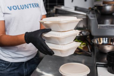 cropped view of young african american social worker holding plastic containers in kitchen