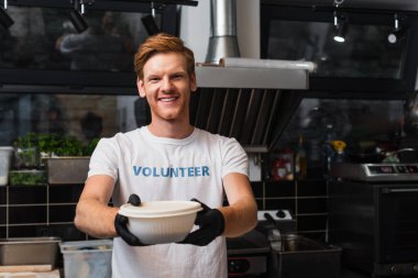happy redhead volunteer offering plastic bowl in kitchen 