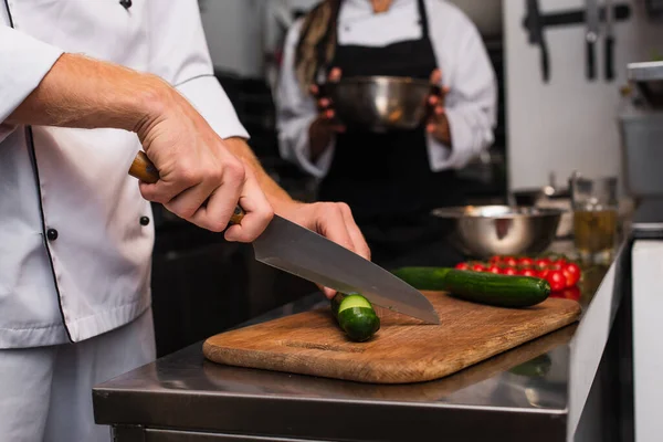 Cropped View Chef Cutting Cucumber Wooden Cutting Board Blurred Colleague — Stock fotografie