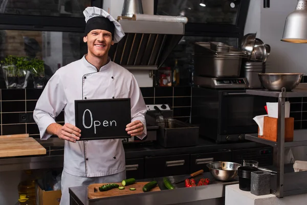 Happy Young Chef Uniform Holding Chalkboard Open Lettering Professional Kitchen — Fotografia de Stock