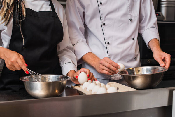 cropped view of chefs holding raw eggs while cooking together in kitchen 