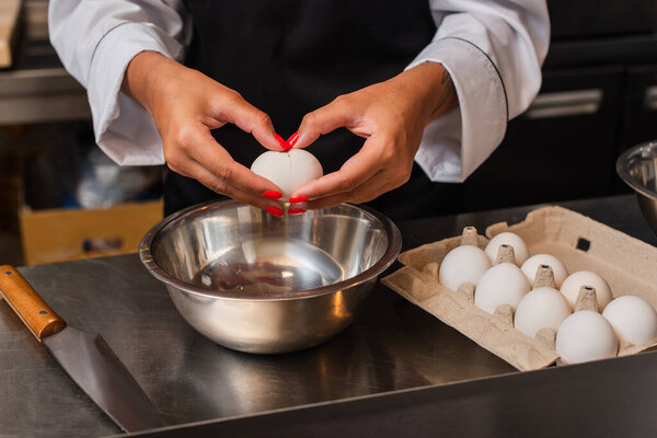 cropped view of african american chef holding raw egg above bowl while cooking in kitchen 