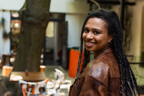 joyful african american woman in brown leather jacket smiling outside