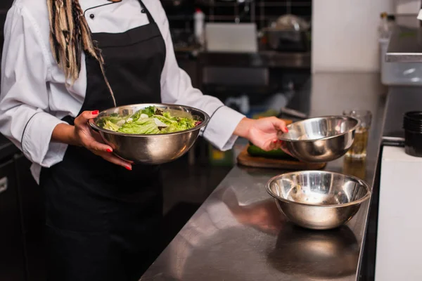 cropped view of african american chef holding bowl with salad in professional kitchen