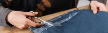 Cropped view of african american craftswoman cutting cloth in workshop, banner 