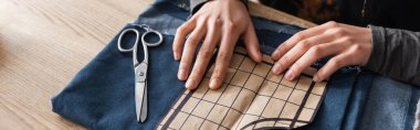 Cropped view of african american craftswoman putting sewing pattern on cloth, banner 