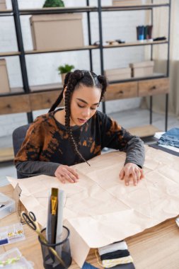 African american designer looking at sewing pattern in workshop 