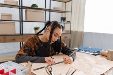 African american designer drawing on sewing pattern in workshop 