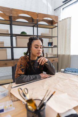 African american craftswoman holding pencil near sewing pattern in workshop 