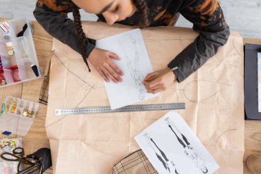 Top view of african american craftswoman drawing sketch on sewing print in workshop 