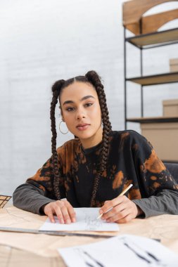 Young african american designer looking at camera while drawing sketch in workshop 