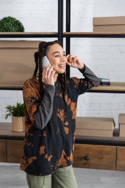 Cheerful african american craftswoman talking on smartphone in workshop 