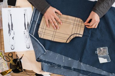 Top view of african american craftswoman holding sewing print near denim cloth and sketch in workshop 