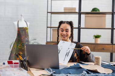 African american designer pointing at sketch during video call on laptop 