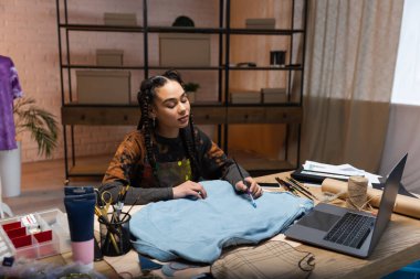 African american craftswoman painting on cloth near devices in workshop 