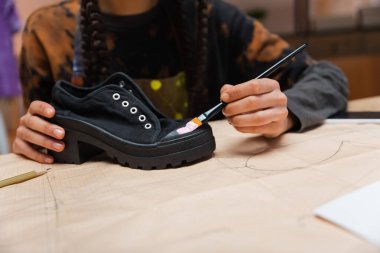 Cropped view of african american craftswoman painting on shoe on sewing pattern in workshop