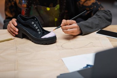 Cropped view of african american craftswoman painting on shoe near devices and sewing pattern 