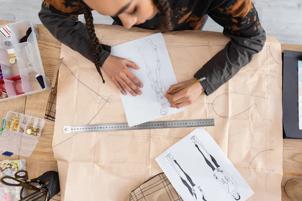 Top view of african american craftswoman drawing sketch on sewing print in workshop 