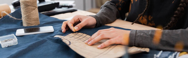Cropped view of african american designer fastening sewing pattern on denim cloth near equipment, banner 