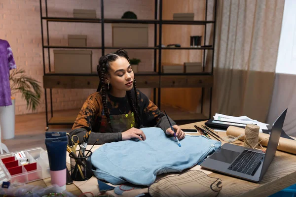 African american craftswoman painting on cloth near devices in workshop