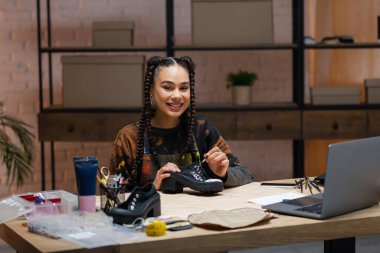 Smiling african american designer painting on shoes near sewing equipment 