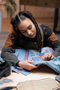 African american designer embroidering denim jacket in workshop 