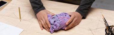 Cropped view of african american craftswoman holding cloth with rubber bands on sewing pattern, banner 