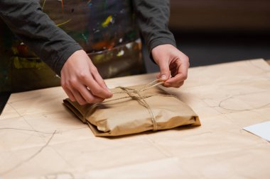 Cropped view of african american craftswoman tying twine on package in workshop 