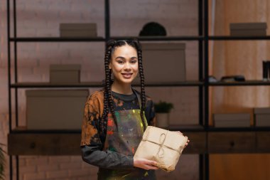 Smiling african american craftswoman holding package in workshop 