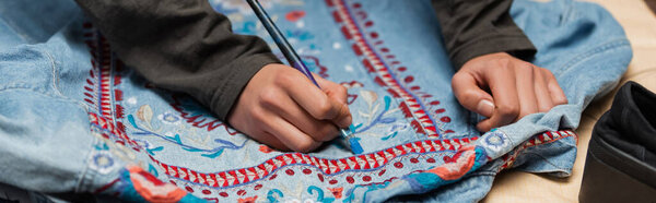 Cropped view of african american craftswoman painting on denim jacket with embroidery, banner 