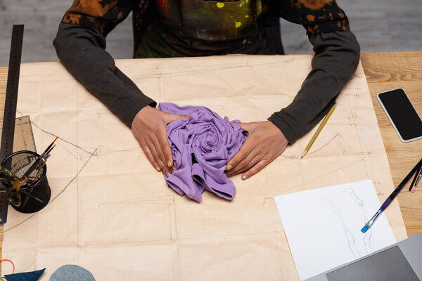 Top view of african american craftswoman holding cloth on sewing pattern near sketch in workshop 