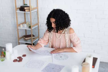 astrologer looking at constellation charts near clay runes and candles