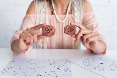 cropped view of blurred astrologer holding clay runes near star charts