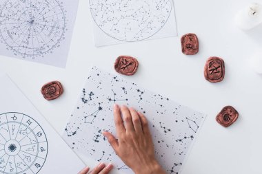 top view of cropped astrologer near celestial charts and clay runes