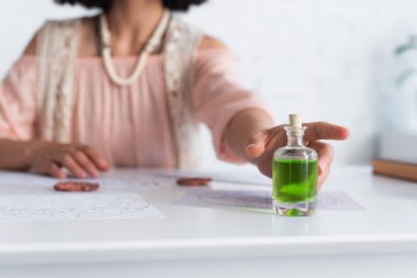 selective focus of bottle with essential oil near cropped astrologer and clay runes