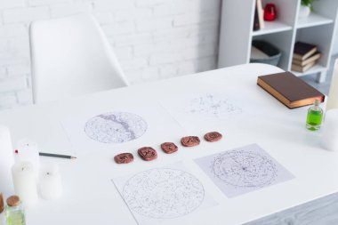 astrological maps and clay runes near candles and prediction book on white table
