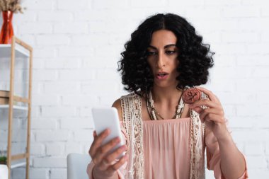 brunette fortune teller looking at mobile phone and holding clay rune